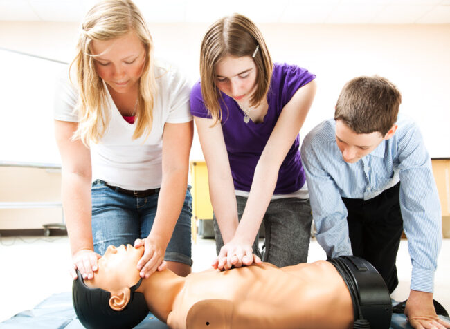 Three students practise CPR on a medical manikin in a classroom setting.