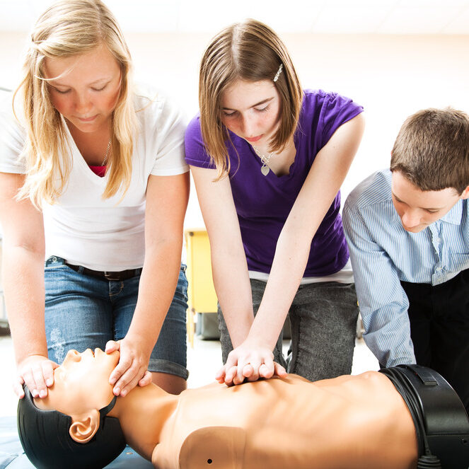 Three students practise CPR on a medical manikin in a classroom setting.