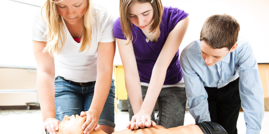 Three students practise CPR on a medical manikin in a classroom setting.