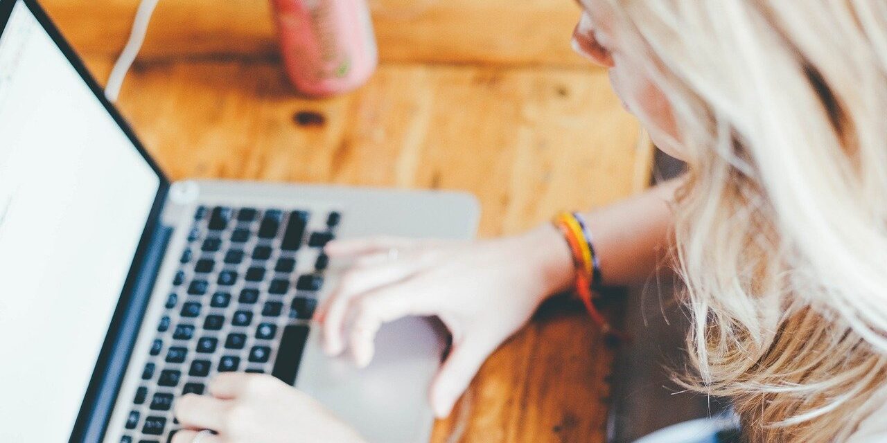 Person typing on a laptop at a wooden table with a drinks can nearby.